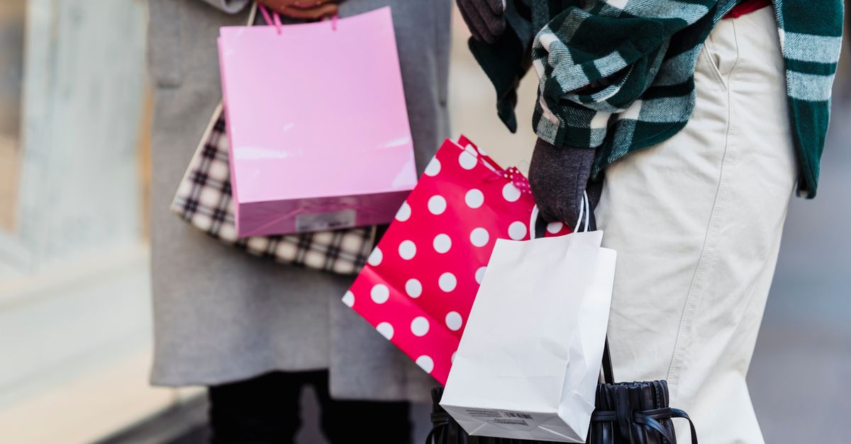 Unrecognizable female friends with various colorful shopping bags standing on sidewalk near showcase on street in city on blurred background